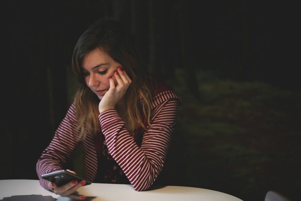 woman leaning on white wooden table while holding black Android smartphone