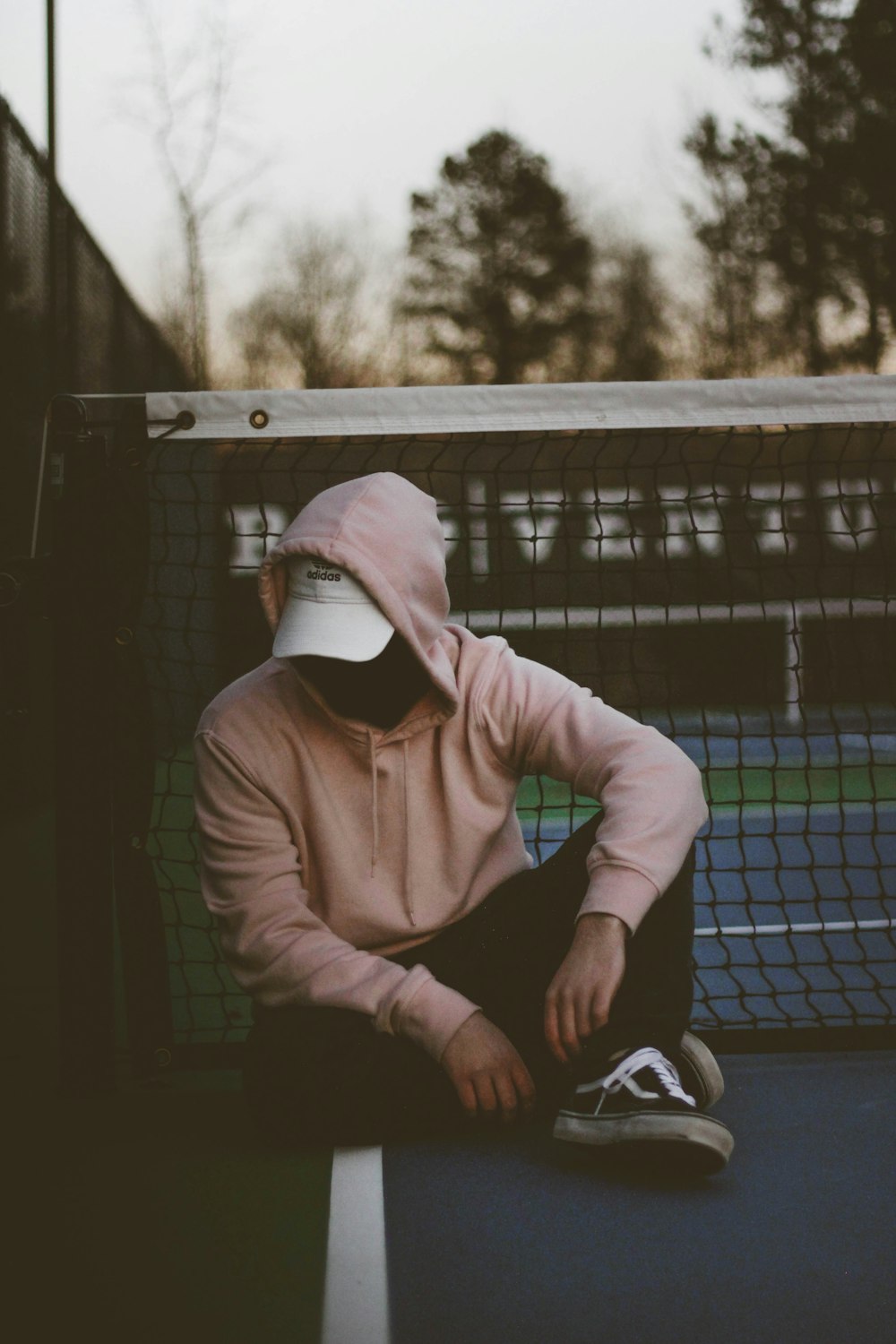 テニスネットの近くに座る茶色のパーカーを着た男