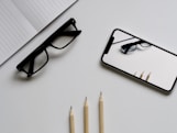 eyeglasses; silver iPhone X; three pencils; notebook flat lay photography