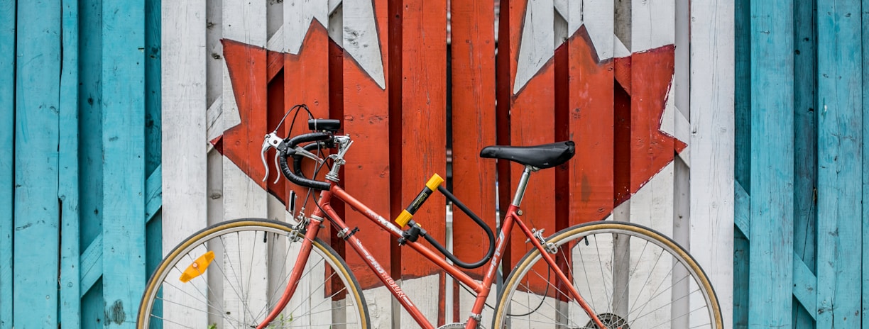 red road bike beside red and white wooden maple leaf painted wall