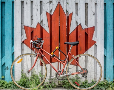 red road bike beside red and white wooden maple leaf painted wall