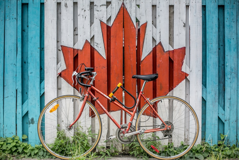 bicicleta de carretera roja junto a la pared pintada de hojas de arce de madera roja y blanca