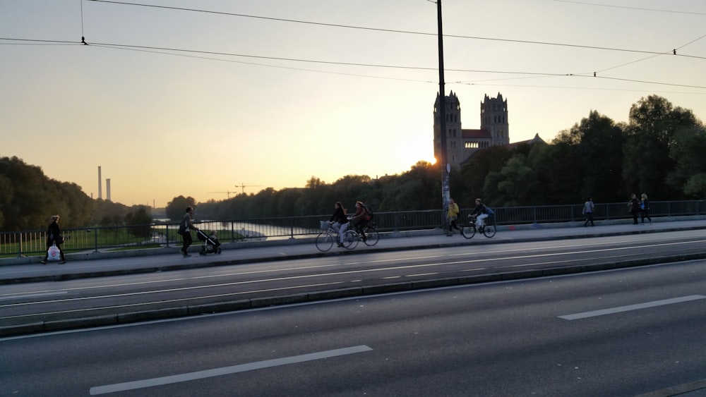 three person riding on bike beside the asphalt road at daytime