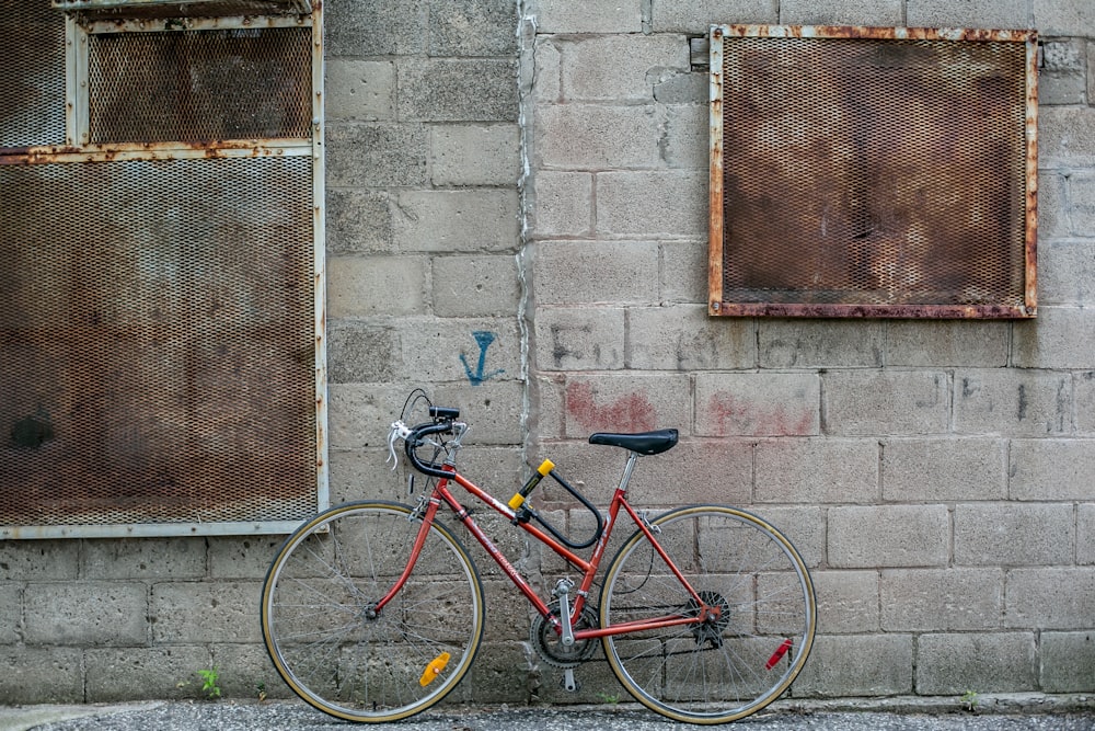 Rotes und schwarzes Rennrad mit Klappgriff, das tagsüber an einer grauen Betonwand lehnt