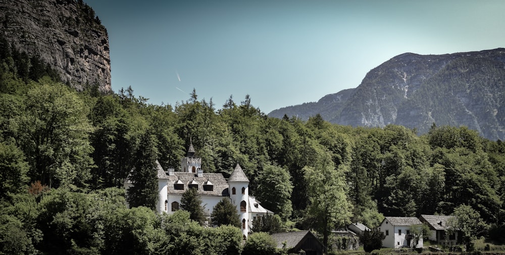 Maison en béton gris et blanc entourée d’arbres à feuilles vertes près des montagnes sous un ciel bleu clair