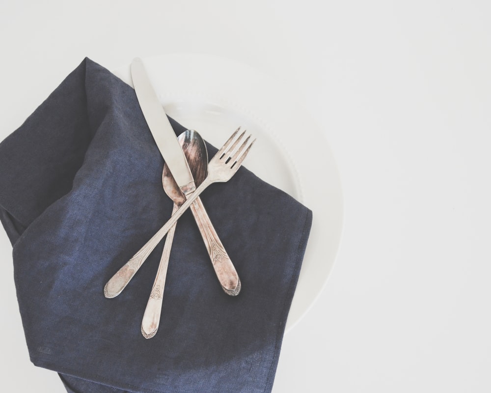 gray fork, spoon, and butter knife on plate with black table napkin