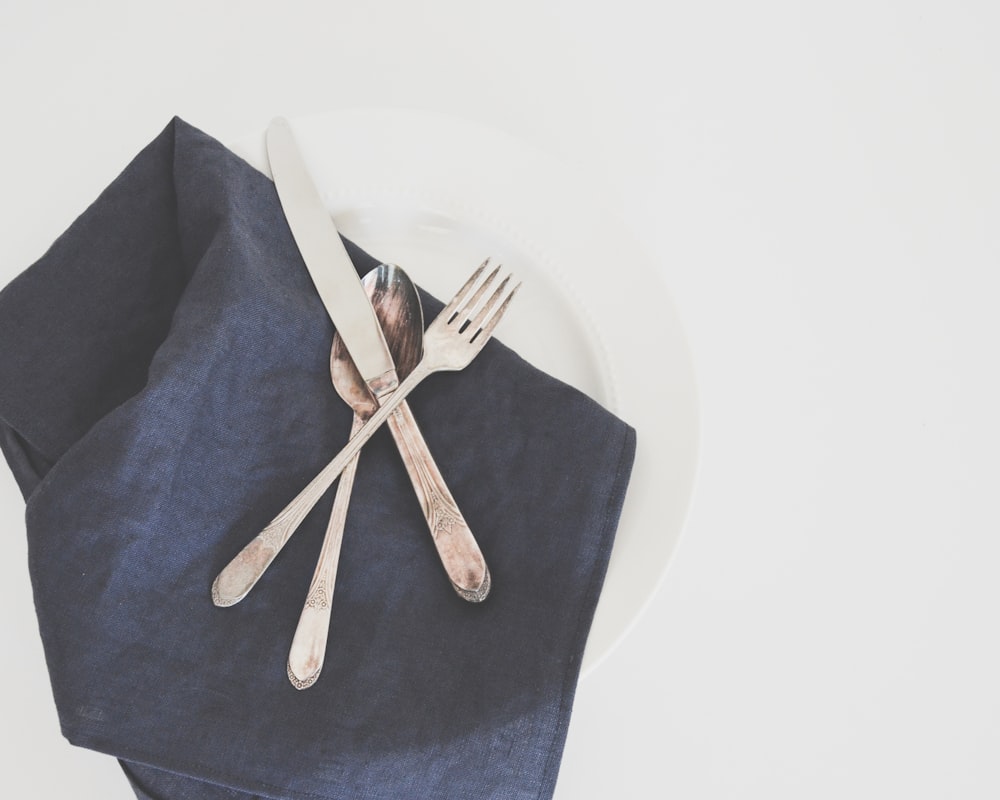 Forchetta, cucchiaio e coltello da burro grigi su piatto con tovagliolo nero