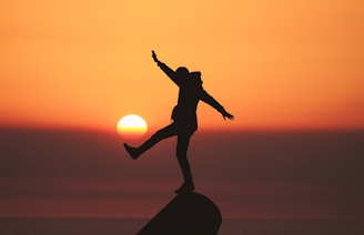 photo of silhouette photo of man standing on rock