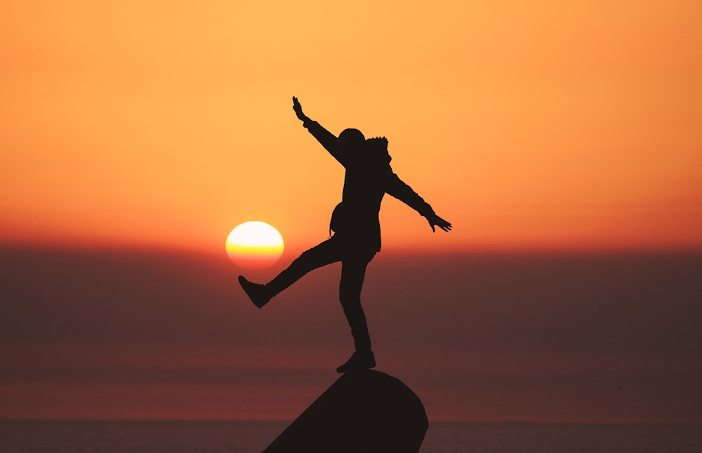 photo of silhouette photo of man standing on rock