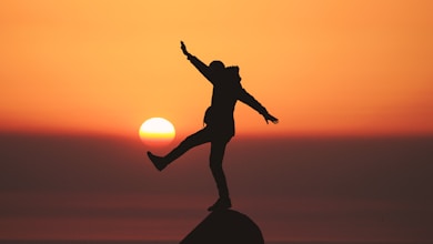 photo of silhouette photo of man standing on rock