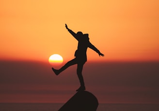 photo of silhouette photo of man standing on rock