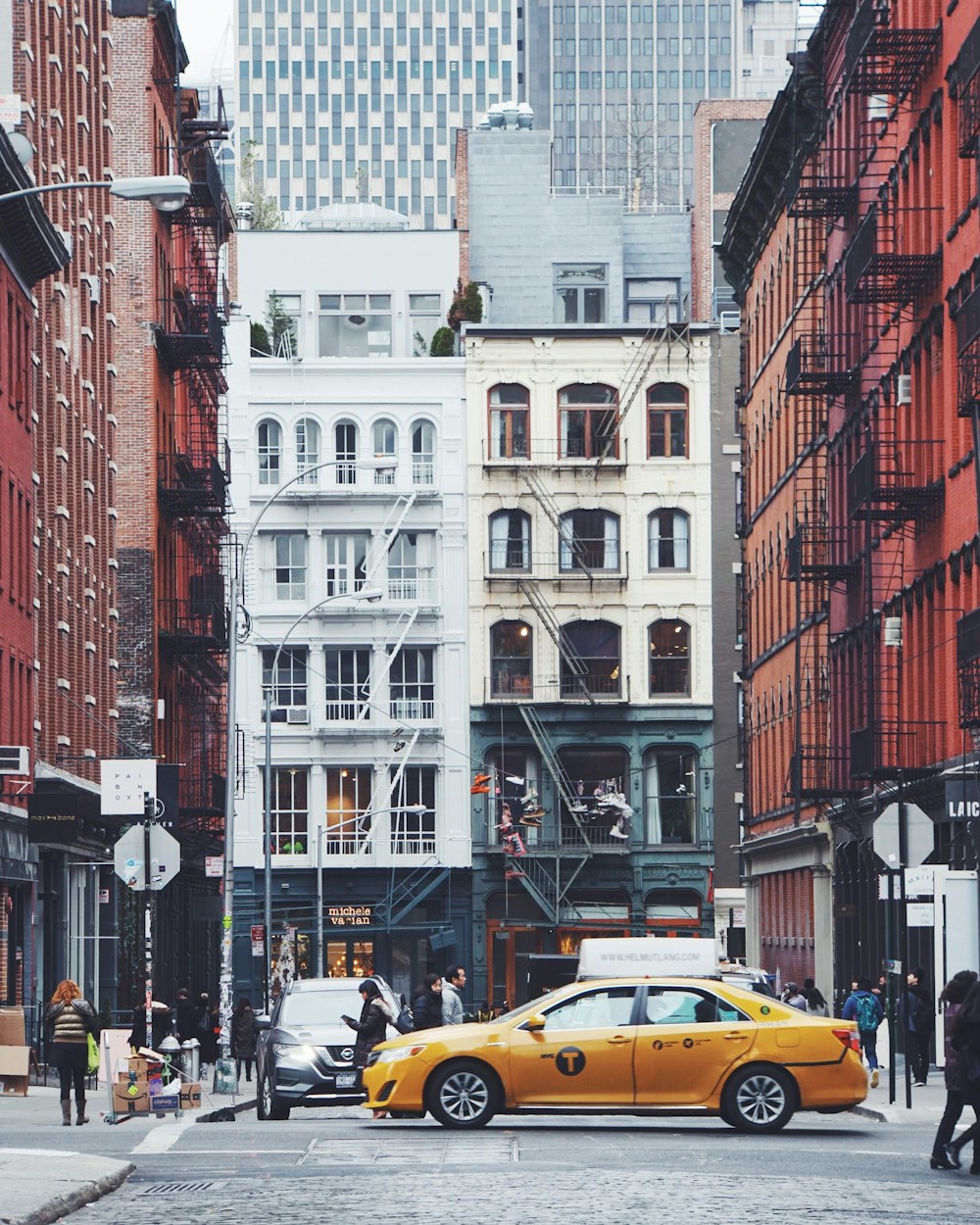yellow sedan on road near buildings with people walks