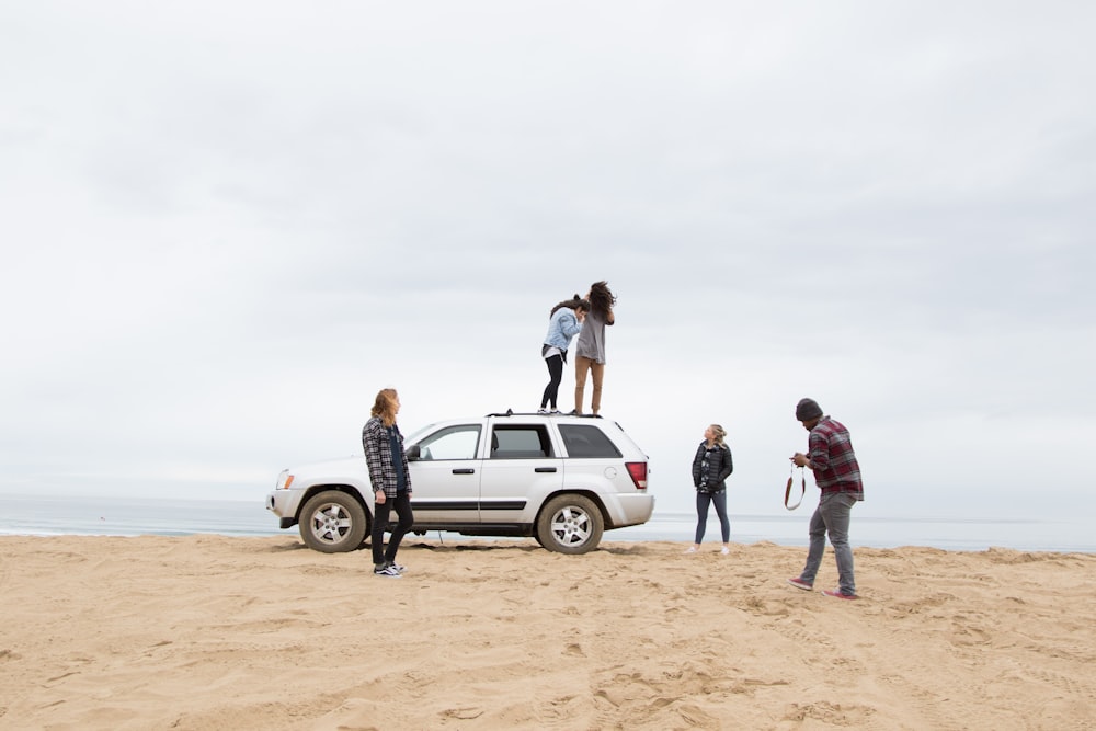 deux personnes debout sur le VUS Jeep Grand Cherokee tandis que l’autre personne filme sur le sable pendant la journée