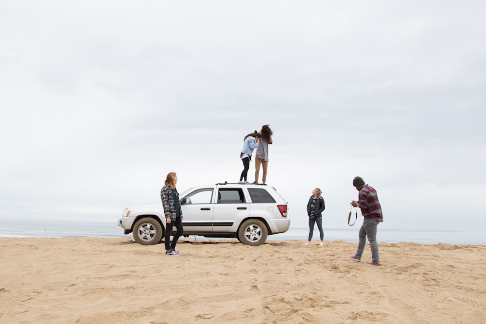 two people standing on Jeep Grand Cherokee SUV while the other person camera on sand during daytime
