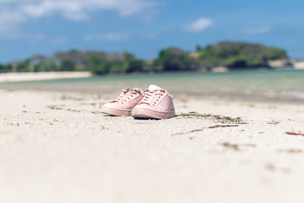 pair of pink shoes on white sand near water during daytime