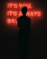 silhouette of woman standing in front of red neon signage low light photography