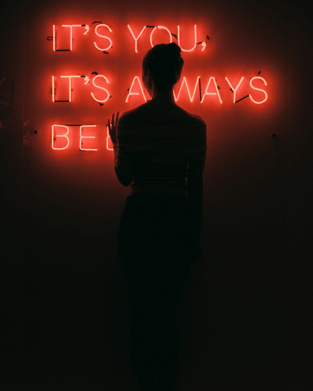 silhouette of woman standing in front of red neon signage low light photography