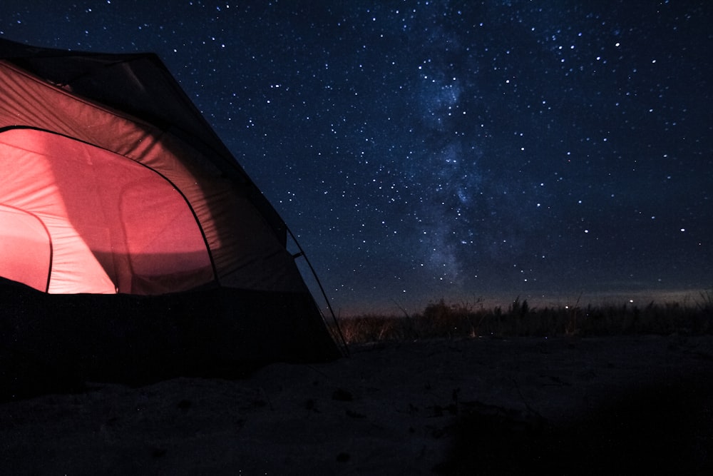 Tienda de campaña de la cúpula roja con luz en el interior bajo el cielo azul con estrellas durante la noche