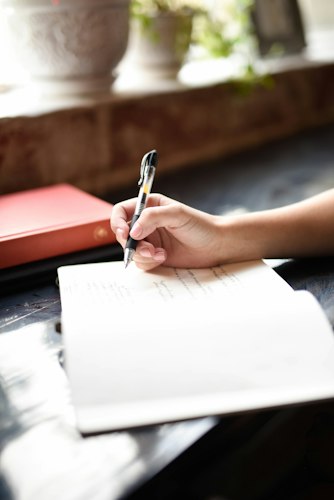 A person journaling by hand at a desk with a laptop open beside the notebook