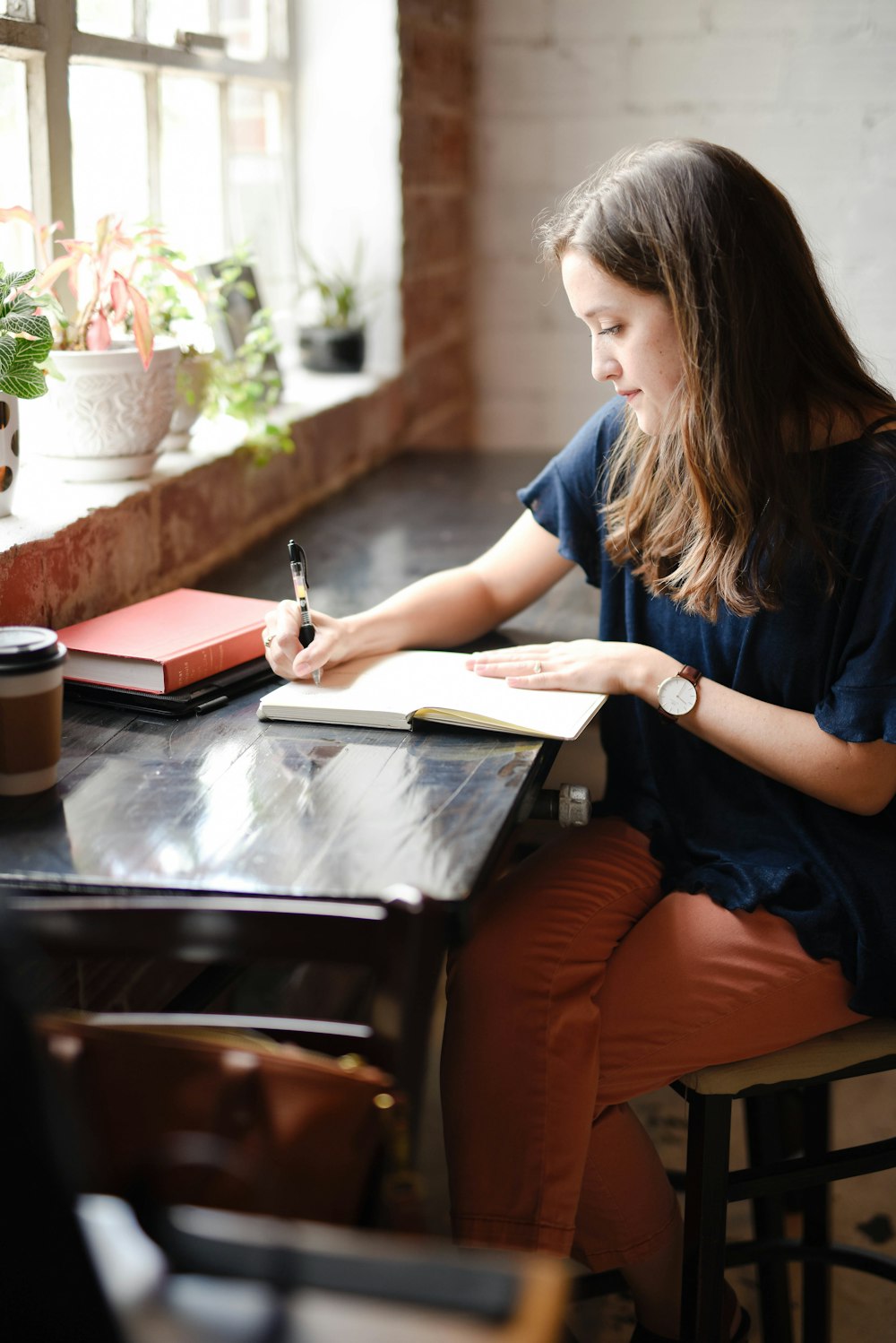 창 근처에 흰색 책에 쓰는 검은 탁자 앞에 앉아 있는 여자