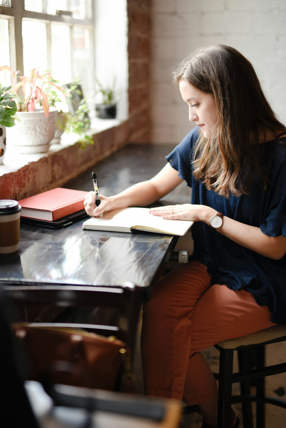 Femme assise devant une table noire écrivant sur un livre blanc près de la fenêtre