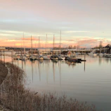 A panoramic view of a calm bay dotted with anchored sailboats at dusk.