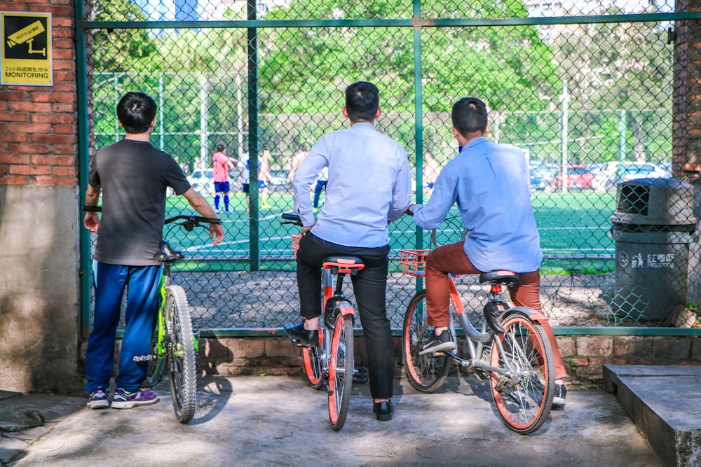 three men sitting on bikes while watching soccer game