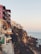 Several modern, multi-story houses are perched on a cliff overlooking the ocean. The architecture features large balconies and terraces, offering expansive sea views. The rocky coastline creates a dramatic contrast with the calm sea and clear sky.