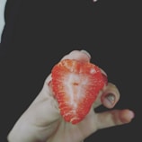 A hand holding a bitten coxinha revealing the juicy strawberry filling inside.