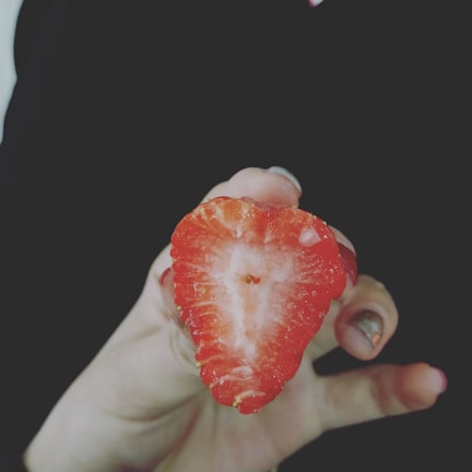 A hand holding a bitten coxinha revealing the juicy strawberry filling inside.