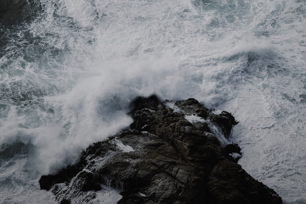 ocean wave splashing on rocky island during day