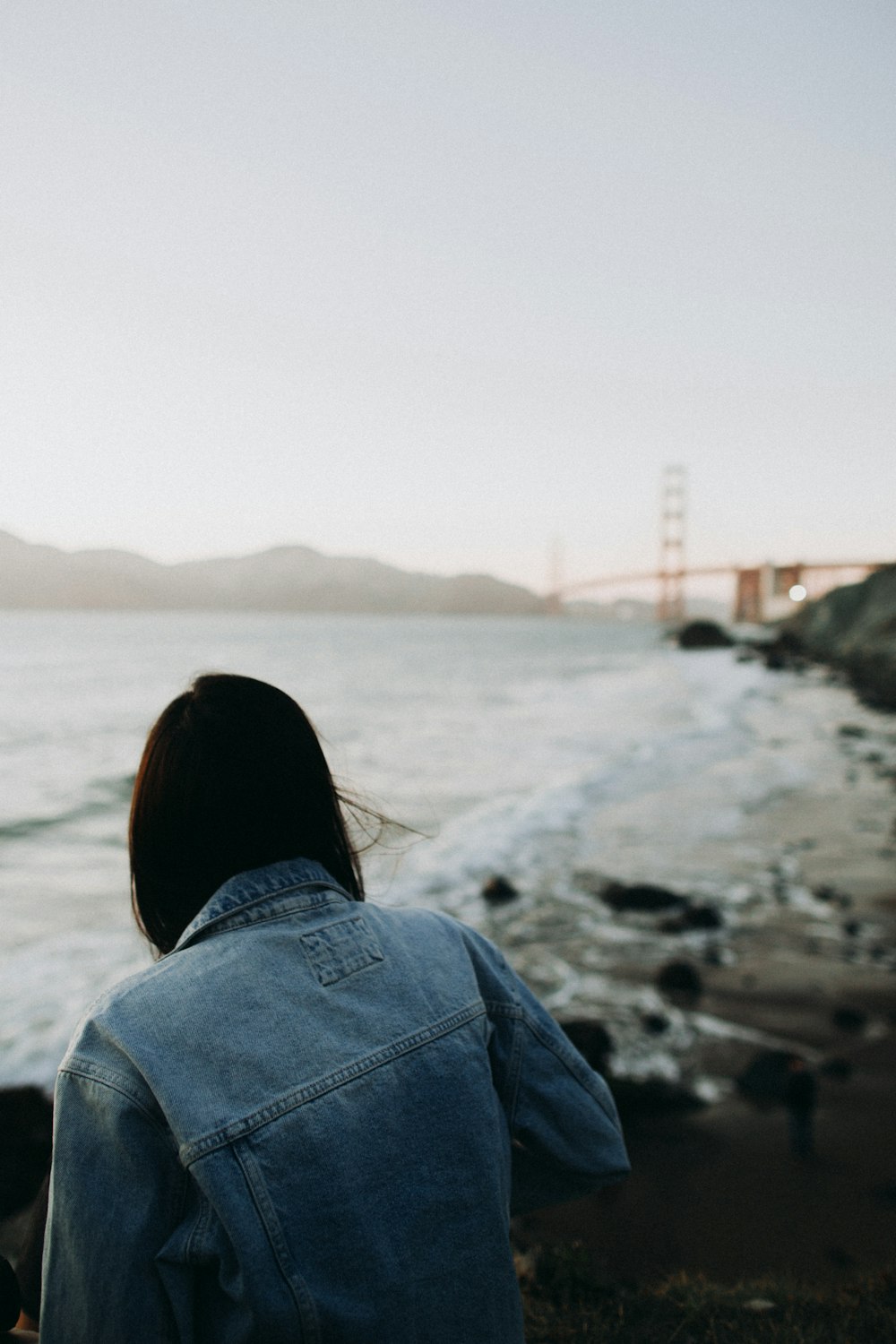 person sitting near sea overlooking red bridge during daytime