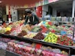 A vibrant market scene featuring a vendor arranging an assortment of colorful candies displayed on a large counter. The varieties include gummies, lollipops, and licorice in various shapes and colors, neatly organized in separate sections. The background shows jars filled with more candy options, enhancing the lively and inviting atmosphere.