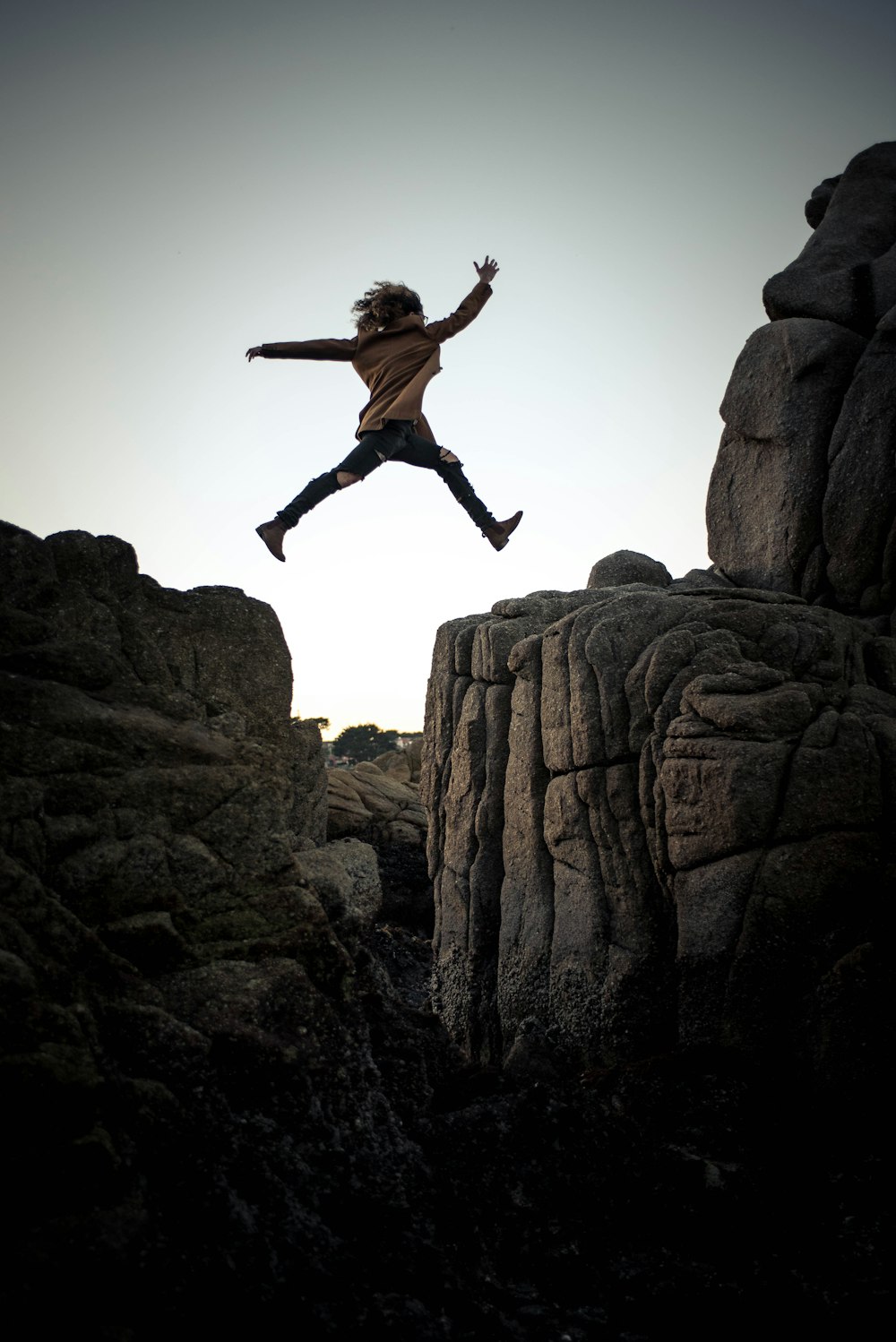 Person, die tagsüber unter grauem und weißem Himmel auf großen Felsen springt