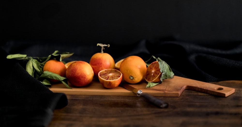 orange fruits on brown wooden chopping board with knife