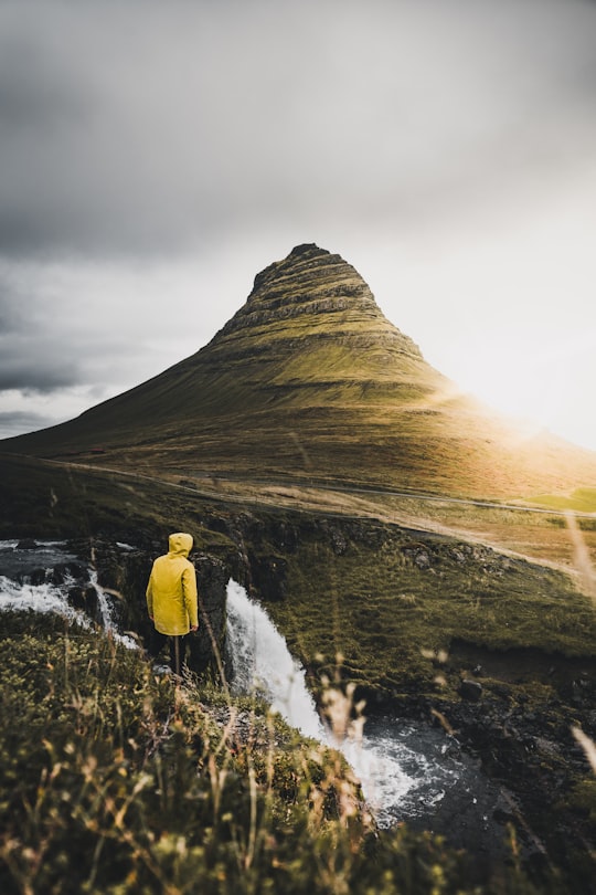 person standing on cliff near waterfalls during daytime in Kirkjufell Iceland