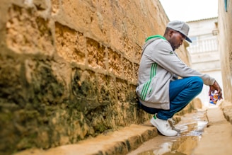 man sitting beside wall during daytime