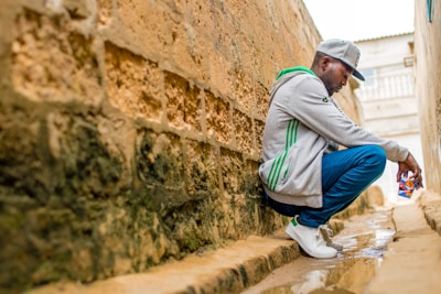 man sitting beside wall during daytime