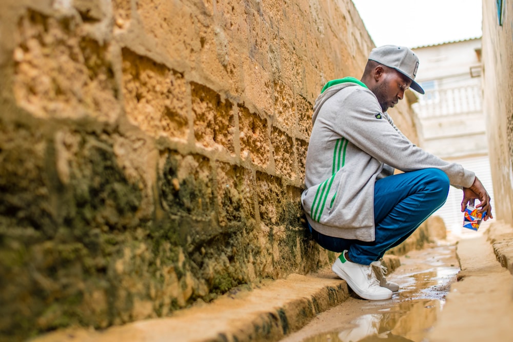 man sitting beside wall during daytime