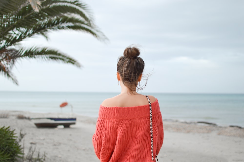 Frau in rotem Strickpullover steht am Strand