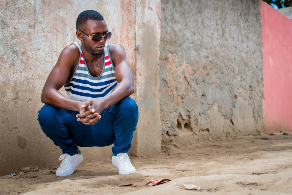 man in white, black, gray, and red striped tank top and blue jeans