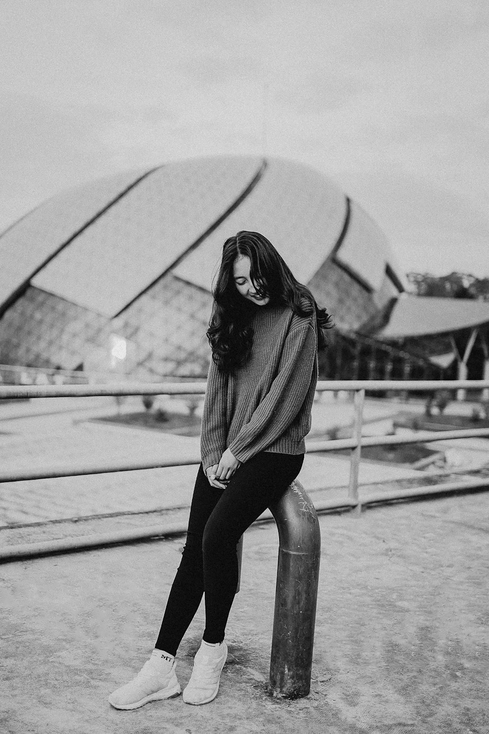 grayscale photo of woman sitting on metal bar