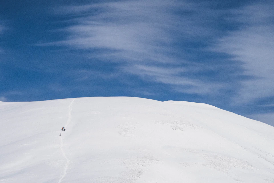 Snowy mountain peak under clear blue sky with fluffy white clouds in foreground