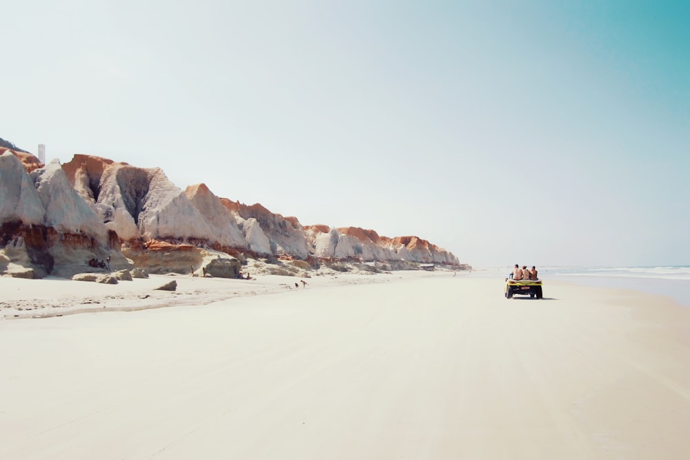 people riding on vehicle near cliff at the seashore