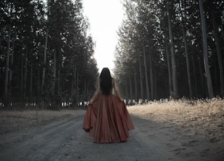 woman holding her brown dress in the middle of forest
