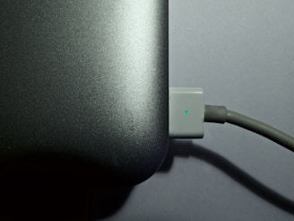 Close-up of a laptop charger plugged into an outlet beside a cozy workspace.