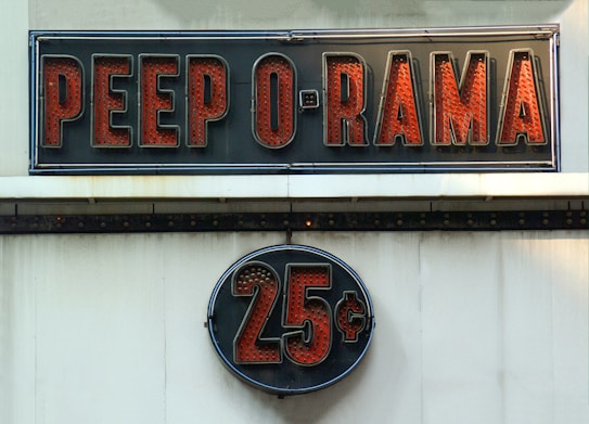 A vintage-style sign reading 'PEEP O RAMA' in large, bold red letters against a black background. Below it, a circular sign displays '25¢' in a similar style. Both signs have a retro, illuminated appearance.