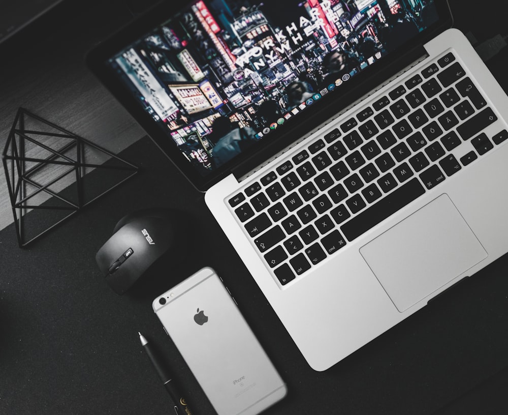 turned on MacBook Pro beside space gray iPhone 6s, black ballpoint pen, and black Asus cordless optical mouse on top of table