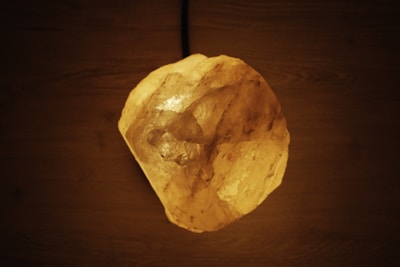 A glowing rock resembling a salt lamp on a dark wooden surface, casting a warm orange illumination.