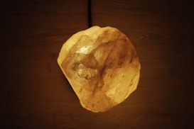 A glowing rock resembling a salt lamp on a dark wooden surface, casting a warm orange illumination.